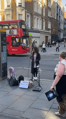 Street musician performs on London sidewalk with illuminated sign