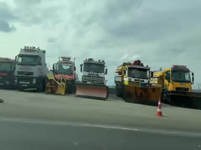 The video shows a view from inside a car driving on a road. At the start, the car passes a construction or maintenance yard with various vehicles, including trucks, a tractor, and portable trailers. The car then passes a traffic light and a small building. Next, the video shows the car entering a tunnel.