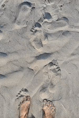 Beachgoer walks along Arambol shore leaving footprints in sand