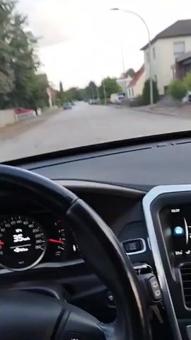 This is a first-person perspective video taken from inside a car, focusing on the dashboard and the road ahead. The driver's hands are visible on the steering wheel. The speedometer shows the car is traveling at a speed of 35 km/h and then 36 km/h. The car's infotainment system displays the time as 08:07, along with radio station information and temperature readings. The exterior view shows a residential street with houses and parked cars. The sky is overcast, suggesting it is daytime. The car appears to be moving forward on the road.