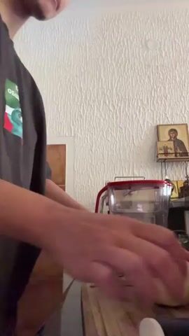 Here is a description of the video. 

A person in a gray t-shirt with a print on it is peeling and chopping an apple on a wooden cutting board. A large knife is being used. A water pitcher is on the counter in the background. An icon is on the wall. Upbeat music is playing.