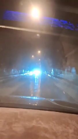 The video shows the interior of a car driving through a tunnel. The road is wet, and the headlights of other vehicles are visible ahead. There are streetlights lining the tunnel walls. The blue strip light in the car's interior roof is visible.