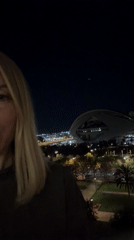 Woman on balcony overlooks illuminated València architecture at night