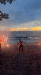 Fire performers and a flaming sign light up Banana Beach at dusk