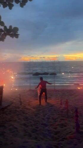 Fire performers and a flaming sign light up Banana Beach at dusk