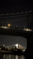 Orange crescent moon rises over a lit Brooklyn Bridge at night