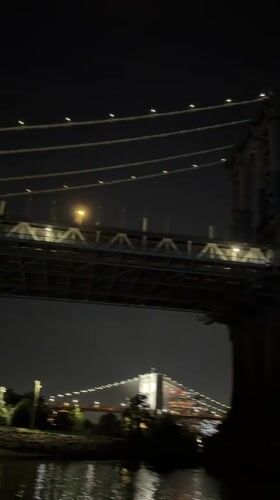 Orange crescent moon rises over a lit Brooklyn Bridge at night