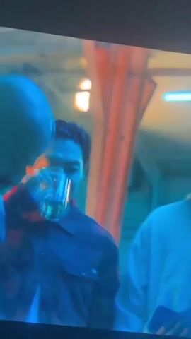 The video features a close-up of a Black man with short dark hair and a beard, appearing to be in an indoor setting. He is wearing a dark jacket over a dark shirt, with a necklace visible around his neck. The scene is characterized by dramatic and artificial lighting, with strong blue and teal tones illuminating much of his face and parts of the background, contrasted by orange, yellow, and red light accents on his face, creating a high-contrast and intense visual.

The man is speaking and reacting to dialogue, displaying serious and intense expressions, which briefly shift to a look of surprise or questioning. The background in the latter part of the video shows vertical stripes of blue and red, suggesting neon lights or a stylized set design.

Visible text overlays on the screen include:
- "You stupid motherfucker."
- "-Ya couldn't help yourself. -What?"
- "Your baby uncle stole that watch from the Halloween"

The video has a cinematic quality, likely from a film or television show.