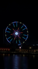 Colorful Ferris wheel lights up an urban waterfront at night