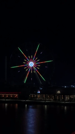 Colorful Ferris wheel lights up an urban waterfront at night
