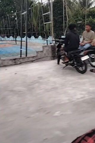 The video shows a blurry, tilted view of an outdoor scene. In the foreground, a person is lying on the ground. There are some motorcycles and trees visible in the background. The overall impression is of a chaotic and unfocused recording.