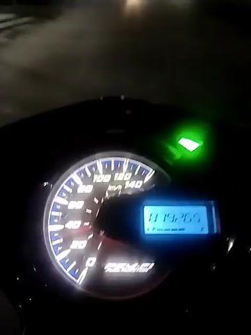 The video provides a first-person perspective from a rider on a motorcycle or scooter at night, with the primary focus on the illuminated dashboard. The dashboard features an analog speedometer with markings up to 140 km/h and a digital display showing "879265". A bright green indicator light, likely a turn signal, is illuminated on the right side of the dashboard. Below the speedometer dial, the word "BEAT" is visible, identifying the scooter as a Honda Beat model.

The vehicle appears to be moving slowly along a road, as indicated by the speedometer needle fluctuating around 10-20 km/h. The background is dark, revealing blurred streetlights and the headlights of other vehicles on what appears to be an urban or suburban street. The time of day is clearly night. No specific weather conditions can be discerned beyond it appearing clear. The sounds of a running engine are audible throughout the clip. The digital reading "879265" likely represents the total distance traveled by the vehicle (odometer reading). The scene is set in Dayahtuha, Indonesia.