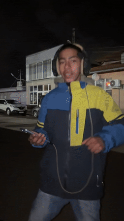 Young man dances with headphones outside Bulgarian cafe at night