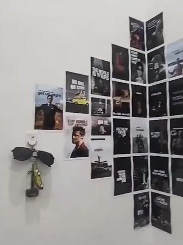 The video shows a wall with numerous posters displayed on it. The posters appear to be motivational or inspirational in nature, with many featuring black backgrounds and white text or images. Some of the posters are arranged in a diamond shape or a slightly staggered grid pattern, while others are placed individually. A small fan is visible on the left side of the wall, mounted at a low height. The wall itself is white and plain. In the lower right corner, there is an electrical outlet with multiple sockets and switches. The lighting suggests an indoor environment. There are no people visible in the video.