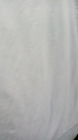 The video begins with a close-up shot of white fabric, possibly a sheet or curtain, exhibiting soft folds and wrinkles. The fabric appears to be illuminated, creating subtle shadows that define its texture. Around the 0:02 mark, the camera starts to move, causing the fabric to blur and shift, hinting at a change in perspective or location. By 0:03, the white fabric rapidly transitions to a blurred view of vibrant green grass, indicating a swift movement or a drop of the camera. The grass fills the frame, remaining blurred for the remainder of the clip, suggesting continuous motion as if the camera is moving quickly over the ground.