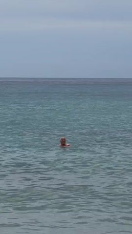 A person with short hair is swimming in the ocean. The water is blue and choppy. The sky is overcast. The person is looking towards the camera.