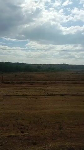 The video shows a dry, brown landscape under a cloudy sky. A line of hills can be seen in the distance, with sparse greenery dotting the landscape. Power lines and poles are visible overhead. There's also music playing during the video.
