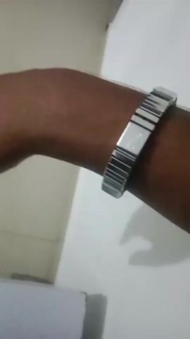 A close-up video shows a person's arm with a silver bracelet on their wrist. The bracelet is made of interconnected metal links with a textured pattern on some of the links. The background is a plain wall with some light and shadow. The video is shot in a way that the bracelet is the central focus.