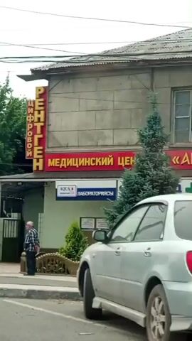 This video captures street scenes in Sokuluk, Kyrgyzstan. The footage appears to be taken from a moving vehicle, offering glimpses of everyday life and the urban environment.

Several people are visible. In the foreground of the first clip, a woman wearing a headscarf and a long skirt stands with her arms crossed, looking to the side. Further in the background of that same clip, another person, possibly a man, is seen standing near a building. In the last clip, two people, one in dark clothing, are walking on a sidewalk near a shop.

Various vehicles are present, including cars and SUVs. One clip shows the side of a white vehicle with a red and blue stripe, possibly a service vehicle. Another clip shows the rear of a beige Mercedes-Benz sedan with a license plate that appears to read "S 4071 AZ". The final clip displays the rear of a red car with a license plate that seems to be "S 0680 F".

The scene is urban, with buildings, power lines, and traffic signs visible. One building has signage in Cyrillic, including "РЕНТГЕН" (X-RAY) and "МЕДИЦИНСКИЙ" (MEDICAL). Another shop sign reads "САЙКАЛ ШОП" (Saikal Shop). Pedestrian crossing signs are also visible.

The time of day appears to be daytime, likely overcast or a cloudy day, as the lighting is diffused. There are no strong indications of specific weather conditions beyond the lack of direct sunlight. The overall atmosphere is that of a casual, ordinary day in a town or city.