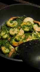 Woman documents cooking shrimp in green sauce in Khimki kitchen