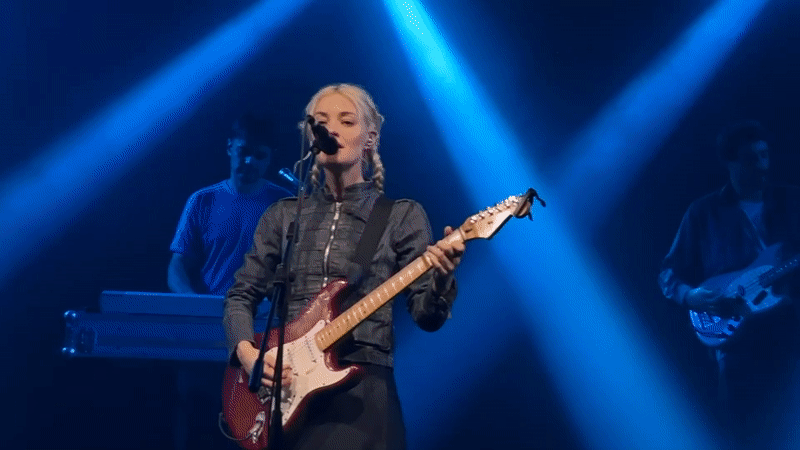 Blonde guitarist performs on Milan stage under blue lights