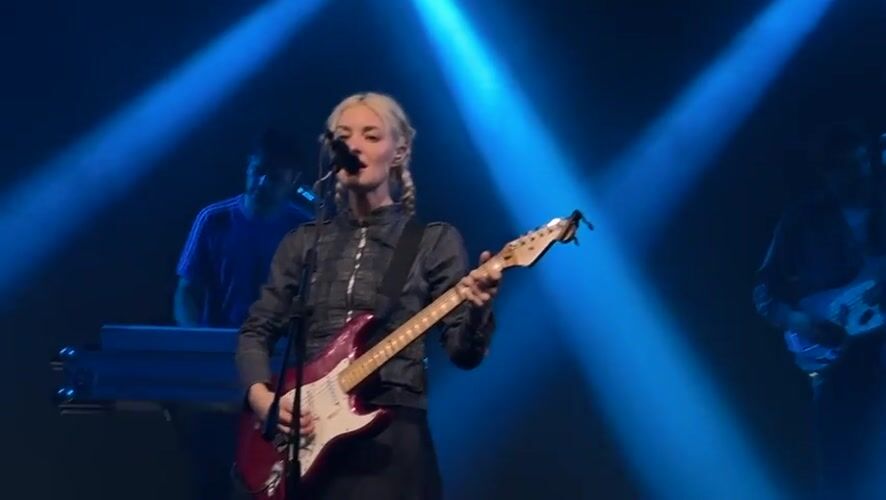Blonde guitarist performs on Milan stage under blue lights