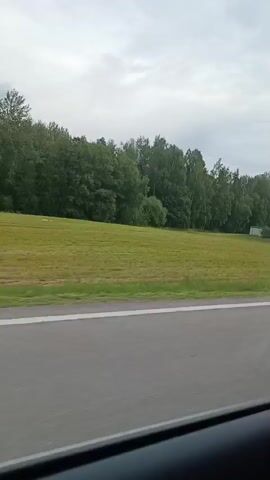 A video recorded from a vehicle shows a tall, red and white metal tower with a large dome on top, possibly a radar or weather station, located in a rural area. The tower is surrounded by trees and a grassy field. The weather appears to be overcast. The video is shot from the perspective of a passenger in a car, with the side of the car visible in the foreground.