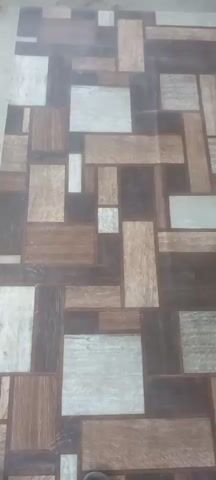 The video shows a close-up view of a floor with a patterned tile design. The tiles are rectangular and square, arranged in an irregular, geometric pattern. The colors of the tiles vary, including shades of brown, gray, and white, with textures resembling wood grain. The lighting is somewhat dim, creating a slightly diffused effect on the surface. The camera appears to be held steady, looking directly down at the floor, with no discernible movement or change in perspective throughout the short clip. No people, objects, or actions are visible other than the floor itself.