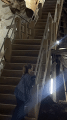 Woman climbs wooden stairs inside cave with makeshift supports