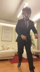 Person in suit and motorcycle gear poses, dances indoors