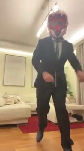 Person in suit and motorcycle gear poses, dances indoors