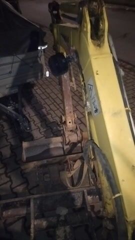 The camera is inside a backhoe looking out at the yellow boom. The camera pans down to reveal two silver levers that the operator uses to control the machine. Then the camera shows a black handle with a light on it.  Next, the camera pans back to show the silver levers and the operator's hand. The operator wears blue pants and grey shoes. The backhoe is parked on a brick patio.