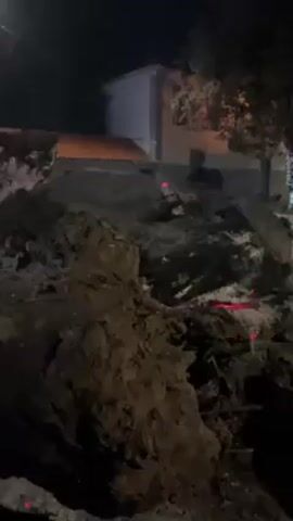 The video begins with a view of a dark and disturbed plot of earth with red lights marking the edges. The camera pans to show people passing by. Then the camera shifts to show a church exterior at night adorned with white and blue lights.