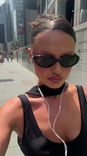 Woman with headphones strolls London sidewalk carrying shopping bag
