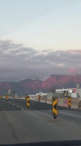 Vehicle travels Paarl road with pink-hued mountains visible