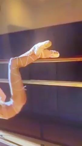 A woman with long brown hair does a pole dance. Her feet are in tan, lace-up boots. She is wearing tan lingerie. She is hanging upside down and holding on to a horizontal pole. The background is dark blue. The camera moves in closer. The lighting is bright and reddish, then gets very bright, obscuring the view.
