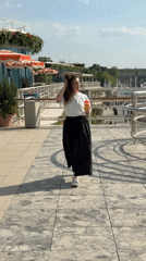 Woman walks sidewalk, drinks on bridge in sunny weather