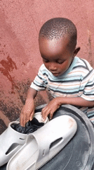 Toddler plays and rests near shoes outside a Jos home