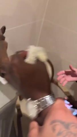 The video appears to be taken in a bathroom.  A person wipes a white, marbled countertop. On the counter are two decorative horse heads, two cups containing what looks like orange liquid and a small object, a small glass, a white container, and a white object that could be an electronic device or tool. A person wearing a bracelet on their wrist is shown giving a plastic bag filled with something to the person wiping the counter. The person taking the video is visible in the mirror. They are holding a phone. Two other people are also visible in the background.