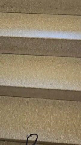 The video shows a staircase and tiled floor. The camera moves up the stairs, which are made of a beige material with a speckled texture. At the top of the stairs, there is a tiled floor. The tiles are also beige with a speckled texture and are arranged in a grid pattern. There is a black border along the base of the wall. The camera moves back down the stairs.
