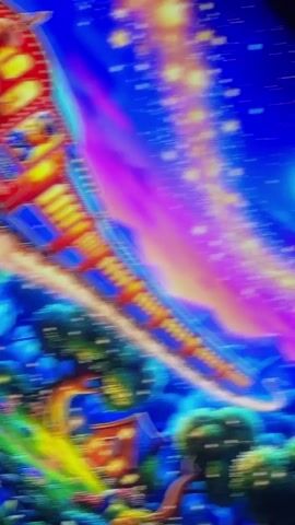 A whimsical, animated scene features a red and blue train with yellow accents, driven by a bear in a blue conductor's uniform. The train is depicted in mid-air, seemingly traveling through a vibrant, starry night sky. Below the train, a fantastical landscape unfolds with rolling green hills, quaint houses with glowing windows, and lush trees adorned with lights. The sky transitions from deep blue to purple and pink hues, filled with a swirling band of golden stars, reminiscent of a galaxy or nebula. The overall atmosphere is magical and dreamlike, suggesting a journey through a fantastical realm. The close-up shots highlight the bear conductor's actions, including waving and looking out from the train's windows.