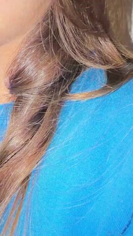 A close-up shot of a person's hair and shoulder, the hair is brown and appears long and slightly wavy, falling over a bright blue shirt. The lighting suggests an indoor environment, possibly with soft light creating subtle shadows. No other details are visible.