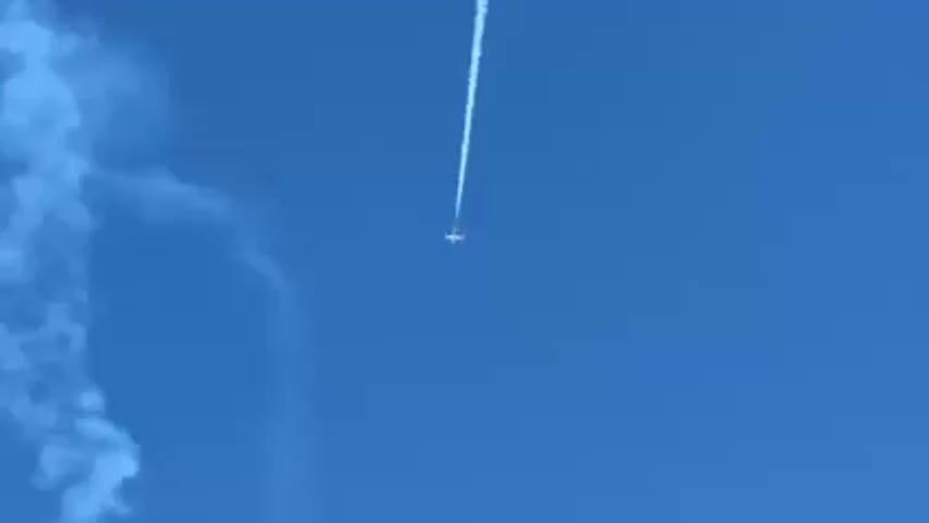 The video shows a small airplane against a clear blue sky. The plane is pulling a white smoke trail behind it. The plane descends vertically and smoke trails are visible on the left.