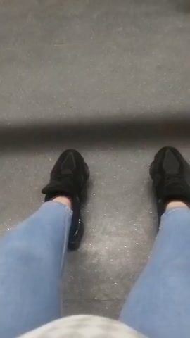 The video shows a first-person perspective of a person's legs and feet. They are wearing light blue jeans and black sneakers. They appear to be standing on a gray surface with some debris.  The camera shakes slightly, possibly due to movement. The sound suggests metal impacting metal.