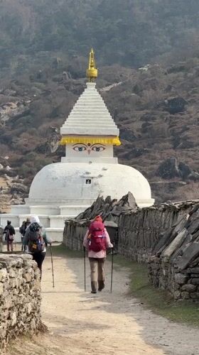 Trekkers pass Buddhist stupa on mountain path in Khumjung