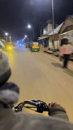 Motorcycle rider travels illuminated Bukuru streets at night