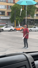 Street performer juggles clubs under umbrella at intersection