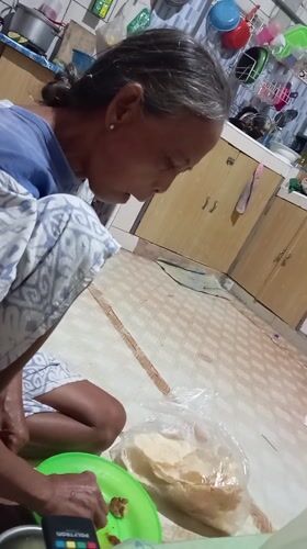 Elderly woman enjoys meal on floor in Baron, Indonesia