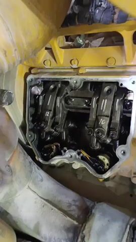 The video shows a close-up view of an engine's valve train. The valve cover has been removed, revealing the rocker arms and valve springs. The engine appears to be a diesel engine, possibly from a heavy-duty vehicle or piece of equipment. The components are coated in oil, which is normal for an engine. The video pans across the valve train, showing several sets of rocker arms and associated components. The lighting is somewhat dim, but the details of the parts are still visible. The environment appears to be a workshop or garage.