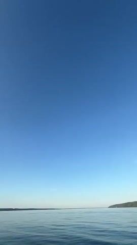This media file captures a serene boat ride on a clear day. The scene opens with a wide shot of a calm, vast body of water under a brilliant blue sky, hinting at an expansive lake or ocean. As the video progresses, the perspective shifts to the front of a small motorboat, showing its bow cutting through the water, creating white frothy wakes.

The time of day appears to be either early morning or late afternoon, as indicated by the gentle sunlight glinting off the water and the soft hues in the sky. The weather is pleasant and clear, with only a few wispy clouds. The boat is moving through tranquil waters, with a distant, tree-lined shoreline visible on the horizon. The overall atmosphere is peaceful and relaxing, evoking a sense of freedom and quiet enjoyment. No people are visible in the video, emphasizing the solitude and natural beauty of the setting. The location is identified as Siukterka, Russia.